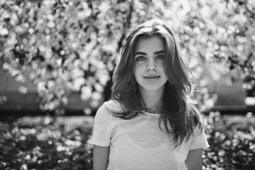 Beautiful young smiling brunette girl in a blooming cherry orchard. Black-and-white picture.