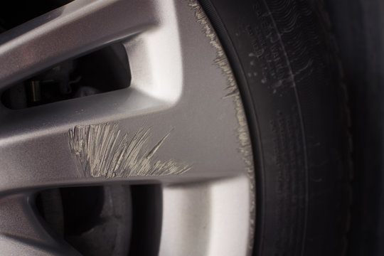 Close up of scratched car alloy wheel rim with curb damage on surface near tire, concept of vehicle maintenance, repair, safety check, and automotive detailing