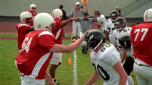 Umpire calling a penalty on football team in white as red team applauds