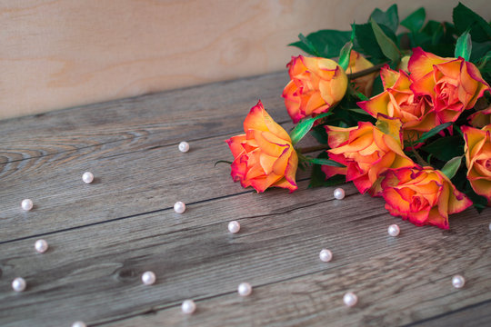 Bouquet of beautiful orange roses on a wooden background and scattered beads of pearls. The best present on birthday. 