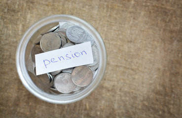 Glass jar filled with coins labeled with the words of the pension. View from above. Background of burlap. The concept of saving money. Accumulating finances