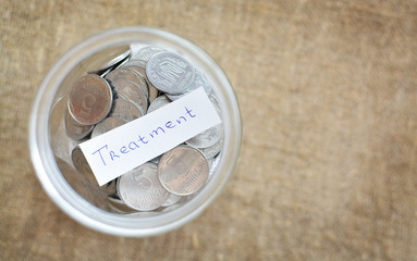 Glass jar filled with coins labeled with words treatment. View from above. Background of burlap. The concept of saving money. Accumulating finances