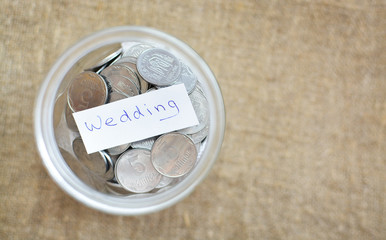 Glass jar filled with coins labeled with the words wedding. View from above. Background of burlap. The concept of saving money. Accumulating finances
