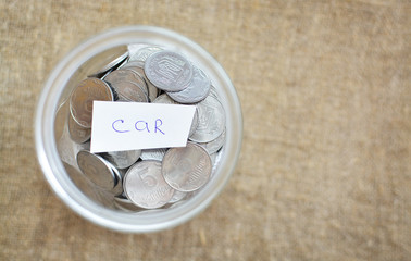 Glass jar filled with coins labeled with the words of the car. View from above. Background of burlap. The concept of saving money. Accumulating finances