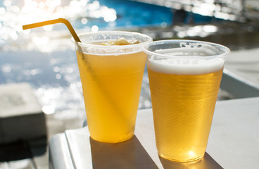 Two plastic transparent glasses with beer stand on a deckchair by the pool. Cooling drink