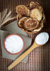 Cooked homemade pancakes on a dining table in a wicker plate next to sour cream for breakfast. Sweet dessert. Homemade cooking. With your own hands. Homemade