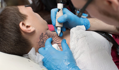 The tattoo artist makes a tattoo on the client's neck in the tattoo salon. The master does a tattoo in the studio. Close-up. Hard. Pain