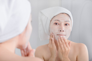 woman applying mask on her face and looking in the mirror