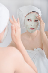 woman applying mask on her face and looking in the mirror