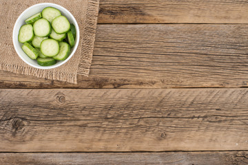 Cut cucumbers in a white bowl on old wooden table.