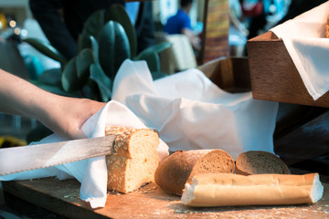 Male hands cutting wheaten bread on the wooden board in breakfast time in hotel. selective focus