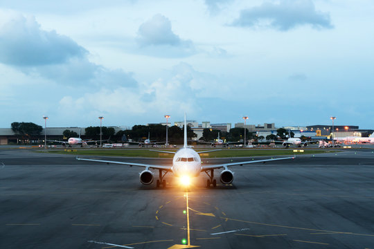 White passenger plane takes off from the airport runway. Aircraft moves against the backdrop of night. Airplane front view.