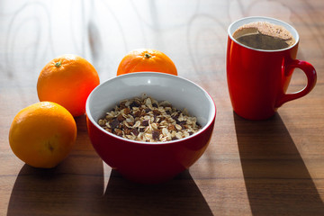 Breakfast with oranges, cereal and steaming coffee in red mug