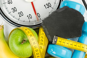 measuring tape green apple dumbbell and empty slate on white bathroom scale fitness concept...