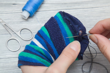 Hand with a needle and thread darning a sock. Handmade. - obrazy, fototapety, plakaty