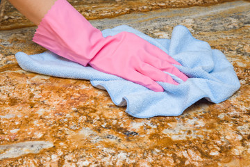 Hand in pink protective glove with rag wiping marble surface. Early spring cleaning or regular clean up. Maid cleans house.