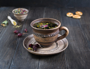 Herbal tea, herbs and flowers in a  clay cup with cookie on wooden table