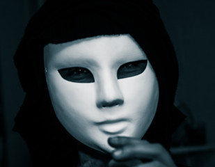 Artistic, monochrome picture of a white carnival mask weared by a woman in darc clothes