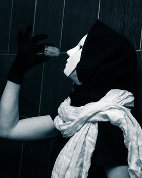 Artistic, monochrome picture of a white carnival mask weared by a woman in darc clothes