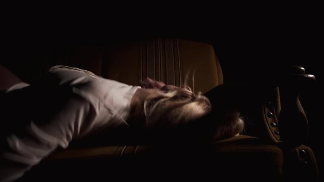 Mentally ill girl lies on a sofa over black background. Her body was tied up threads. She tries to get rid of them