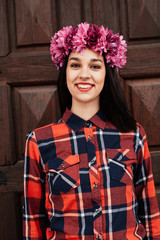Pretty stylish girl with pink flower crown in front of a wooden door