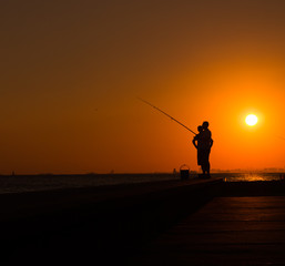 Silhouettes of fishermen by the sea at sunset