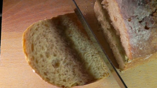 View from above on slow motion of knife cutting off a loaf grain bread