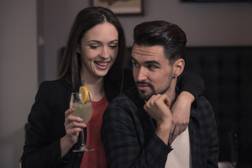 young woman hugging man, looking at camera smiling pub drinking cocktail closeup
