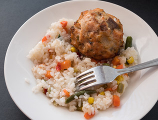 Fish cutlet with a side dish of rice on dark background.
