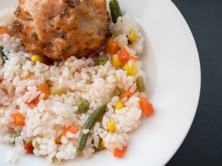 Fish cutlet with a side dish of rice on dark background.