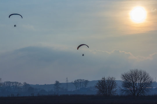 paramotor glider flying in the sky over beautiful countryside field landscape at sunset