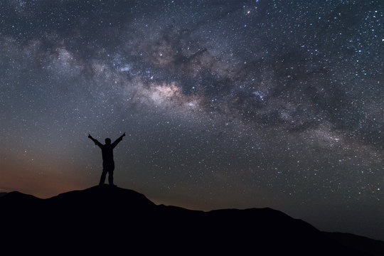 Milky Way landscape. Silhouette of Happy man standing on top of mountain with night sky and bright star on background.