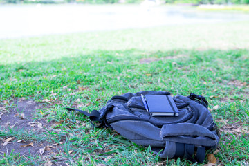 Notebook and a pen is placed on black backpack in shady tree in the garden with holiday.