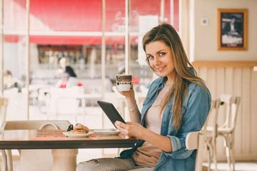 Cute girl reading e-book one in the cafe and drinking coffee with pastries
