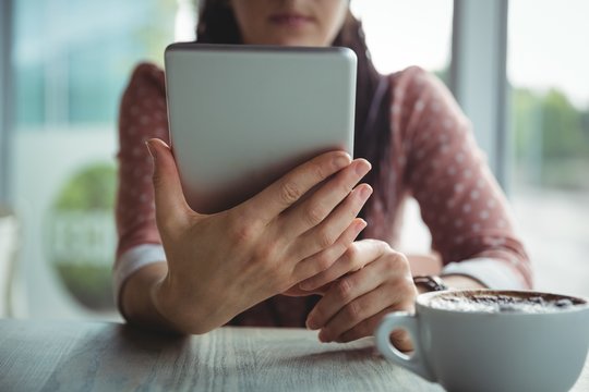 Woman using digital tablet while having cup of coffee