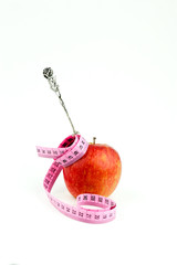 silver pastry fork in apple wrapped with measuring tape. Diet concept.