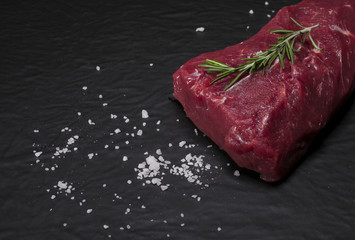 Raw beef steak on a cutting board with rosemary and spices.