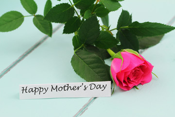 Happy Mother's day card with one pink rose on blue wooden surface
