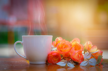 White coffee cup and rose flowers on wooden table with blurred background.