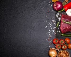 Raw beef steak on a cutting board with rosemary and spices.