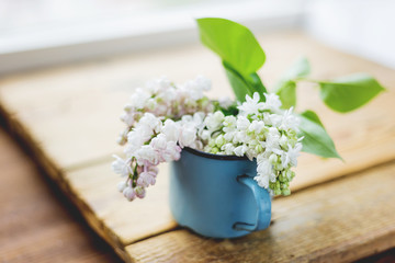 Lilac (Syringa) flowers in old rusty mug. Spring background with white and violet flowers in rustic cup on wooden table.