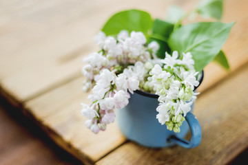 Lilac (Syringa) flowers in old rusty mug. Spring background with white and violet flowers in rustic cup on wooden table.