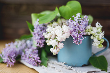 Lilac (Syringa) flowers in old rusty mug. Spring background with white and violet flowers in rustic cup on wooden table.