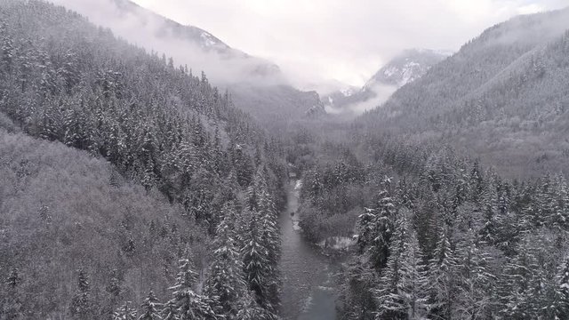 4K Helicopter View of Gray Fog on Forest Mountain Tops with Snow Flakes Falling on Valley River