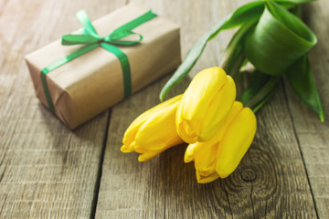 Obraz na płótnie Canvas Three yellow tulips and gift box on wooden table