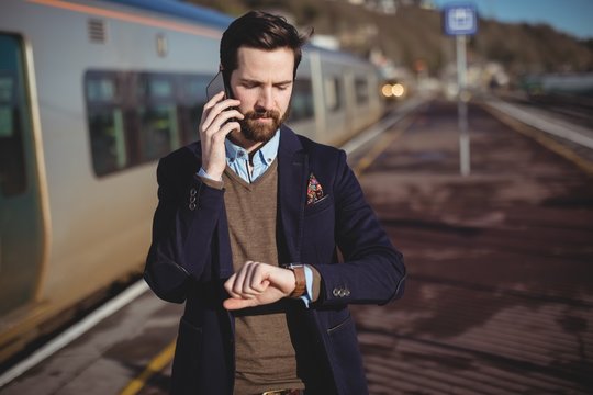 Businessman checking time while talking on mobile phone