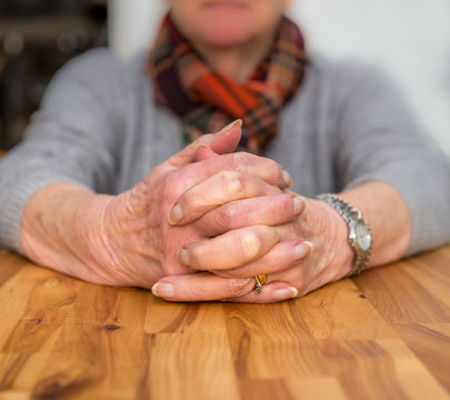 Clasped hands of an elderly lady sitting at a table.