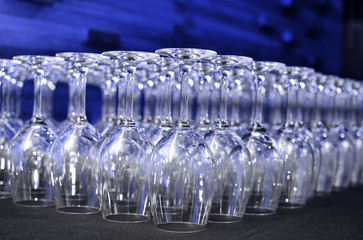 Upside down wine glasses on bar in row with blue lights in background