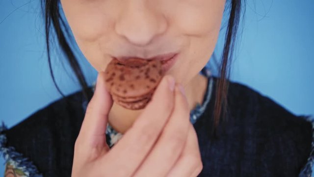 Close up front view, unrecognizable brunette girl with big smile and white healthy teeth bites cacao chocolate macaron cookie, isolated on sky blue background