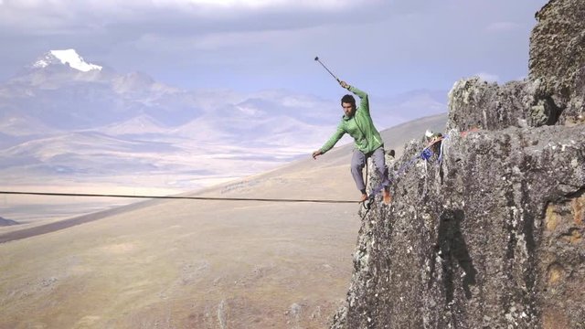 Slackliner balancing on tightrope between two rocks, Snowy mountains of the Huascaran park on the background, Peru. Slow motion